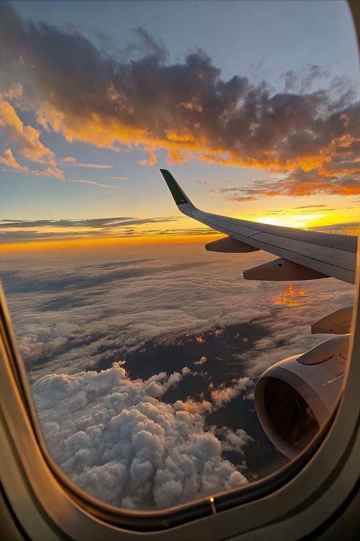 Vue depuis un hublot d’avion au coucher du soleil, au-dessus des nuages